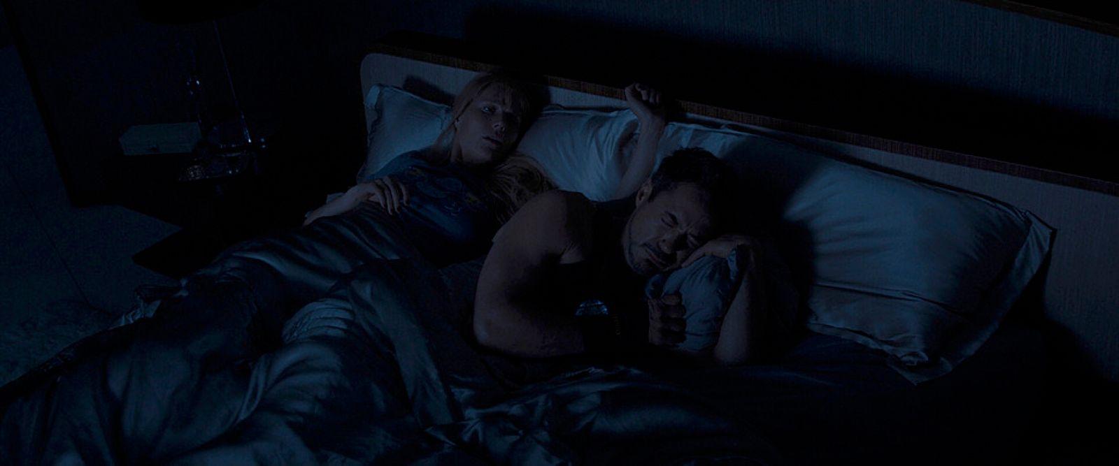 a man and a woman laying in bed in the dark