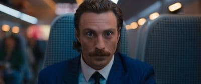 a man in a suit and tie sitting in a train