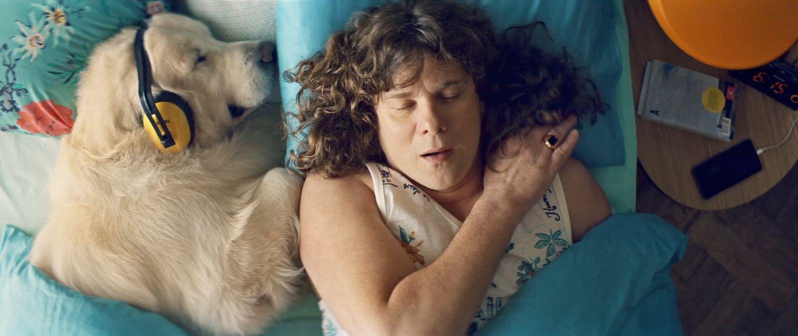 a woman laying in bed with a dog wearing headphones