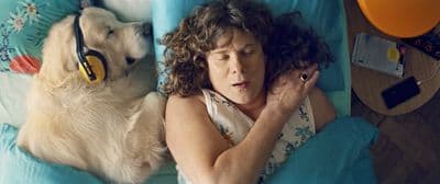 a woman laying in bed with a dog wearing headphones