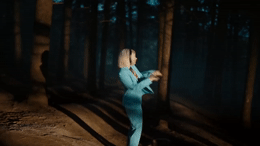 a woman in a blue suit is dancing in the woods