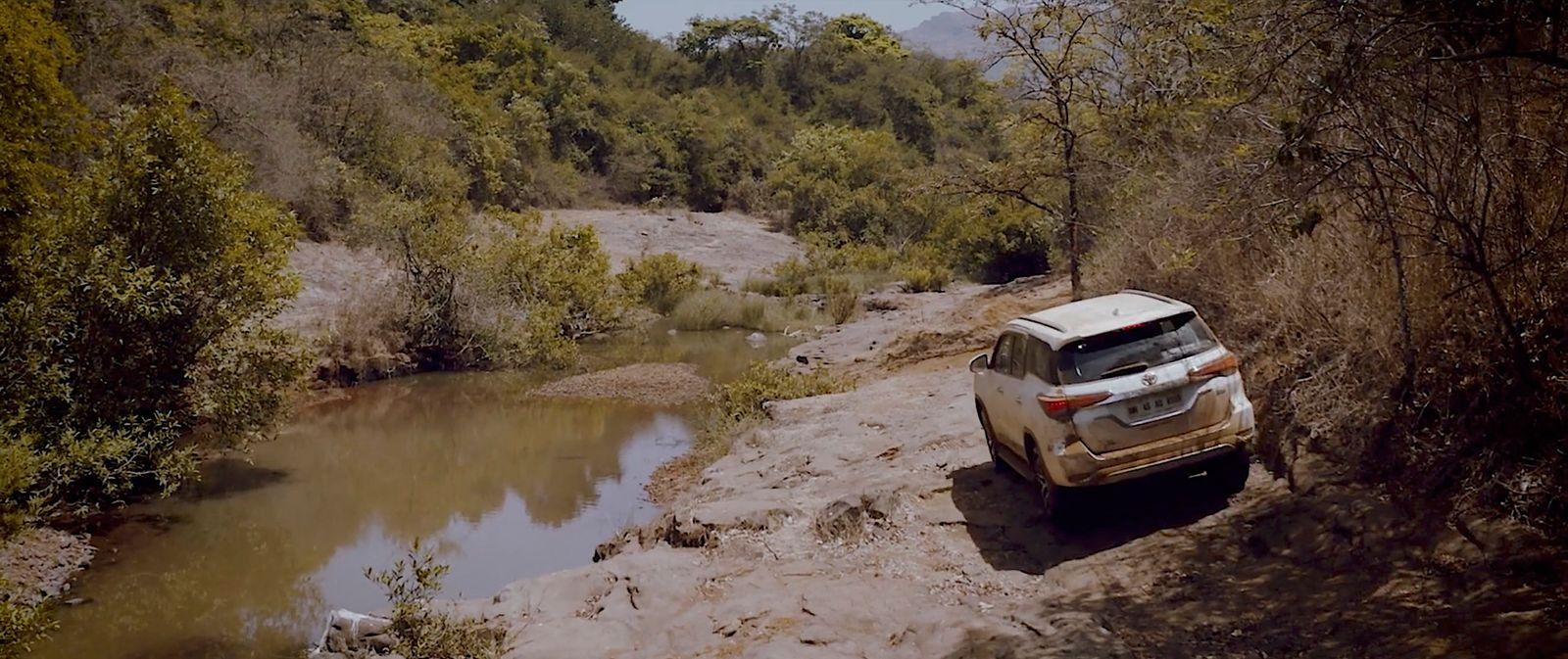 a white suv driving down a dirt road next to a river