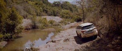 a white suv driving down a dirt road next to a river