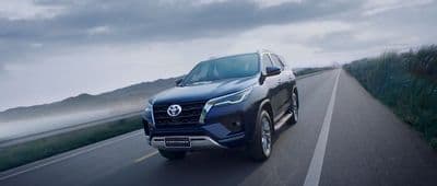 a blue suv driving down a road next to a body of water