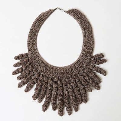 a crocheted necklace is displayed on a white surface