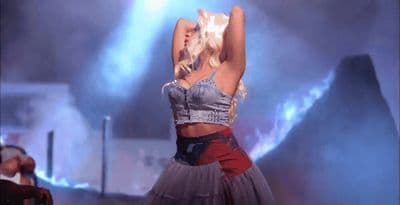 a woman in a skirt on stage with her arms in the air