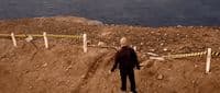 a man standing on top of a dirt hill next to a body of water