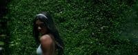 a woman standing in front of a lush green hedge