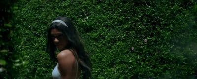 a woman standing in front of a lush green hedge