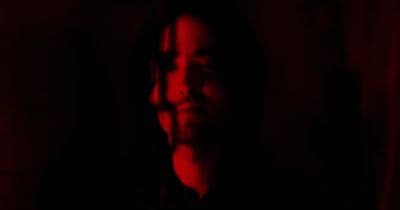 a man with long hair standing in a dark room