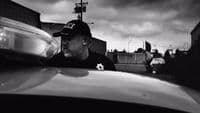 a black and white photo of a man leaning on a car