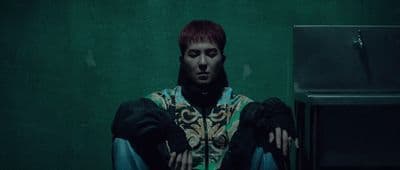 a man with red hair sitting in front of a green wall