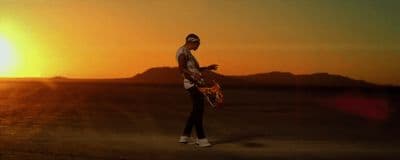 a man standing in the middle of a desert holding a skateboard