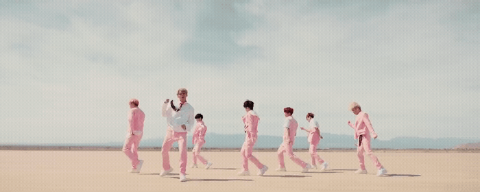 a group of men in pink suits walking across a desert