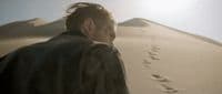 a man standing in front of a mountain with footprints in the sand
