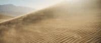 sand blowing in the desert with mountains in the background
