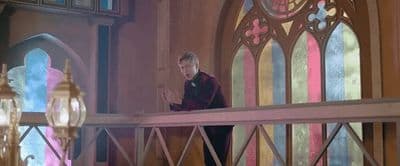 a man standing on a balcony next to a stained glass window