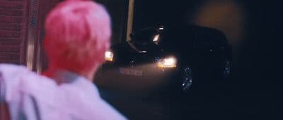 a woman with pink hair standing in front of a car