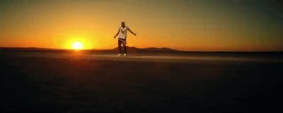 a man riding a skateboard across a field at sunset