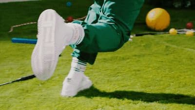 a person in green pants and white sneakers kicking a frisbee