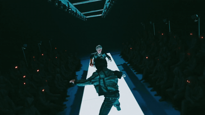 a man walking down a runway in a dark room