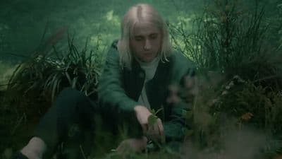 a woman sitting in the grass with her hands on her knees