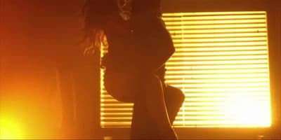 a woman standing in front of a window with the sun shining through the blinds