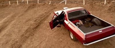 a red pick up truck parked on a dirt road