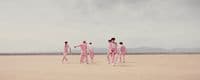 a group of people in pink suits walking across a desert