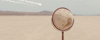 a mirror sitting on top of a metal pole in the middle of a desert