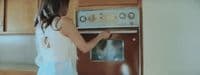 a woman is opening the oven door in a kitchen