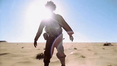 a man walking across a desert covered in sand