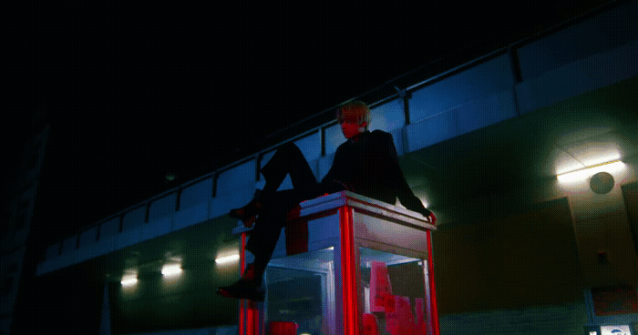 a man sitting on top of a red box in front of a building