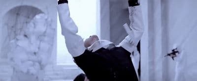 a man in a white shirt and black vest holding his hands up in the air