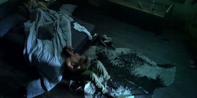 a shirtless man laying on a bed in a dark room