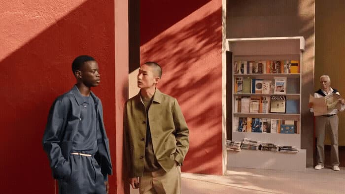 two men standing next to each other in front of a red wall