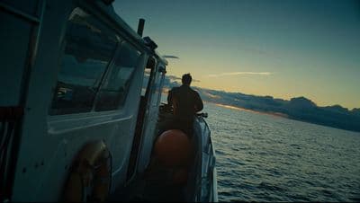 a man standing on the back of a boat at sunset