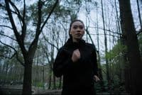 a woman in a black jacket is running through the woods