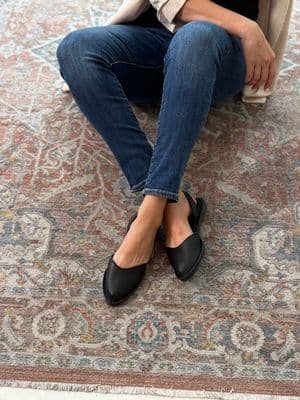 a woman sitting on a rug wearing black shoes
