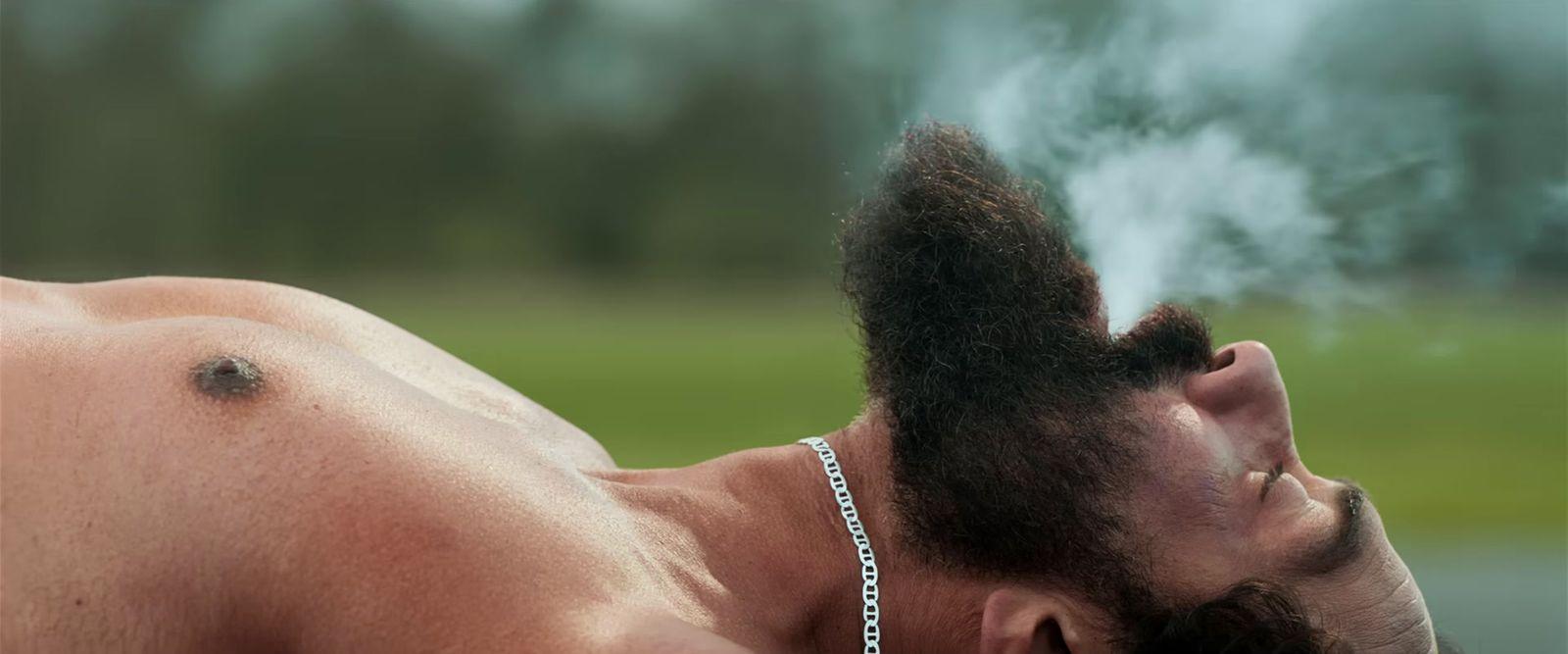 a shirtless man with a chain around his neck smoking a cigarette