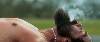 a shirtless man with a chain around his neck smoking a cigarette