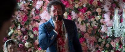 a man in a suit and tie standing in front of a flower wall