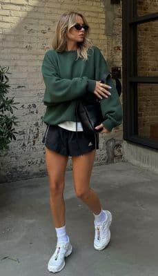 a woman wearing a green sweater and black shorts