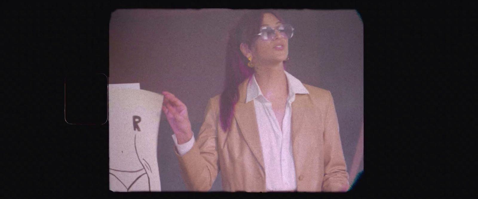 a woman in a suit and glasses standing in front of a black background