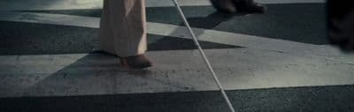 a person walking across a cross walk with a cane