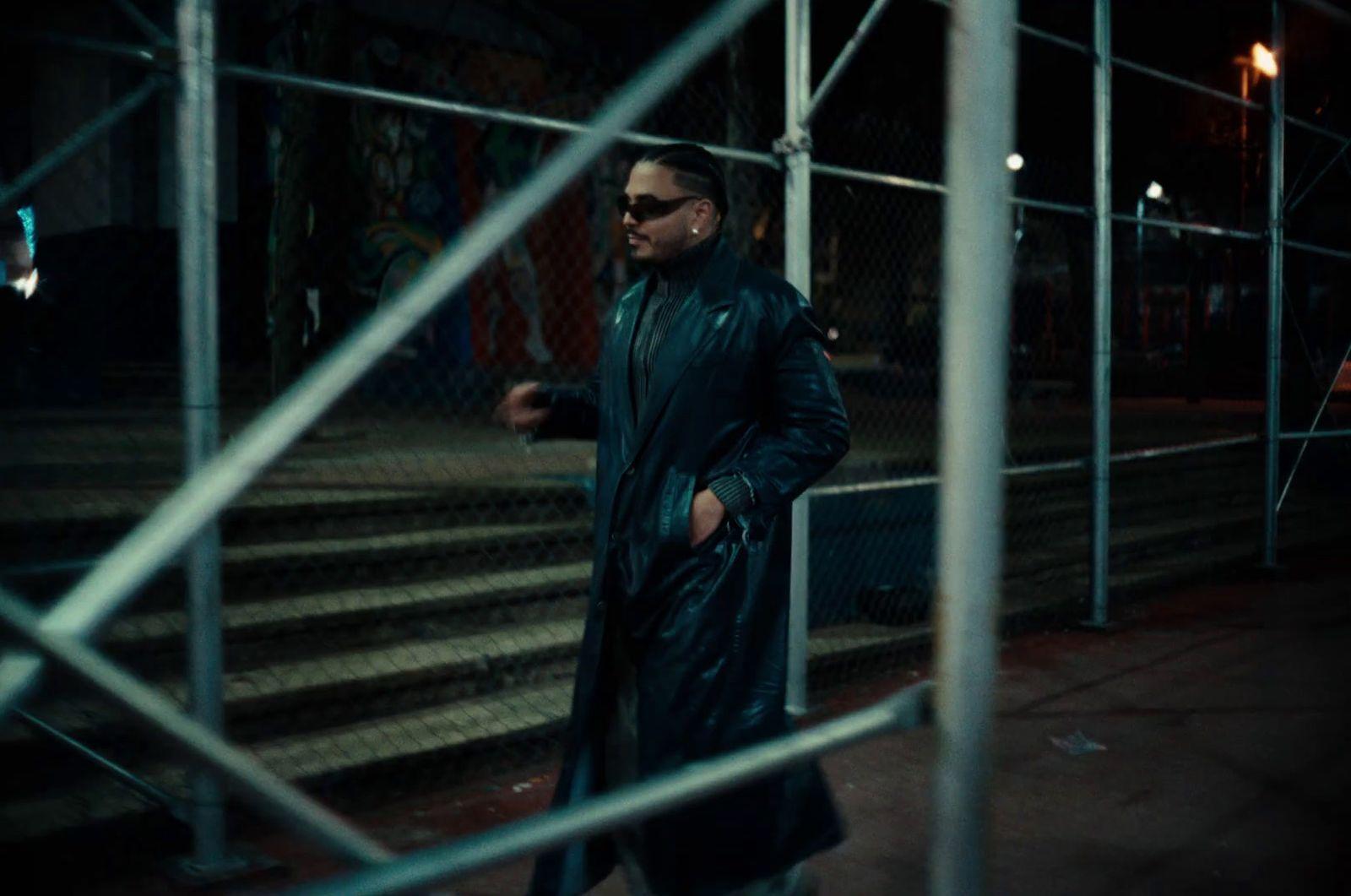 a man in a black coat and sunglasses walking down a street