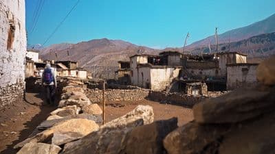 a man walking down a dirt road next to a stone wall