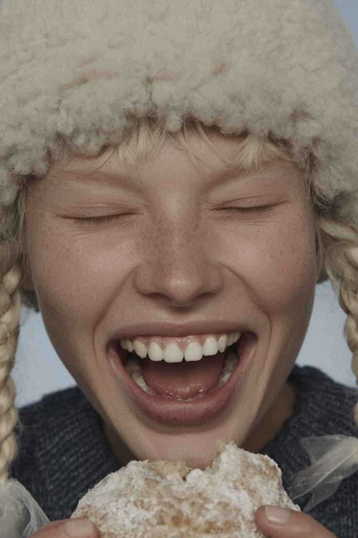 a young girl wearing a hat and eating a doughnut