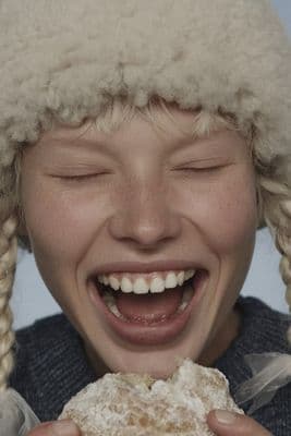 a young girl wearing a hat and eating a doughnut