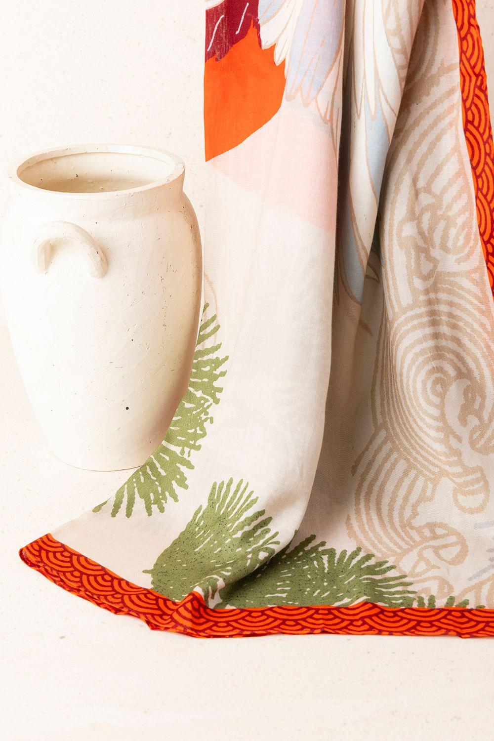 a white vase sitting on top of a table next to a scarf